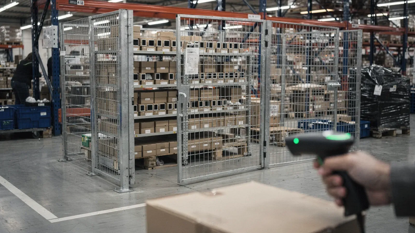 Cage grillagée fermée contenant des appareils électroniques en boîte, scanner code-barres au premier plan.