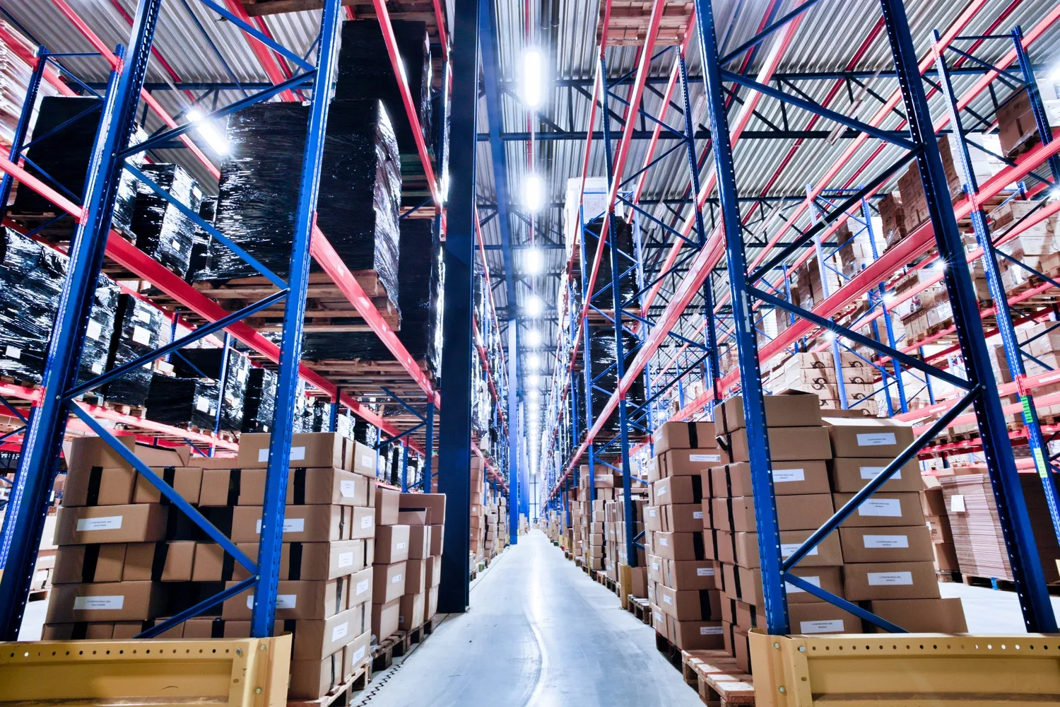 Allée de racks palettes dans l’entrepôt de Houdeng-Goegnies, cartons prêts pour la préparation.